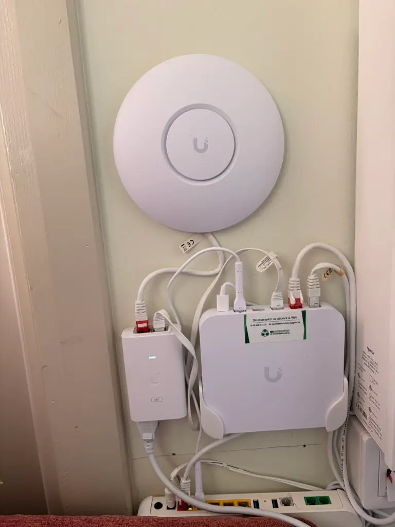 UniFi-accesspunkt på väggen ovanför Cloud Gateway Ultra och PoE-adapter på Djurgården