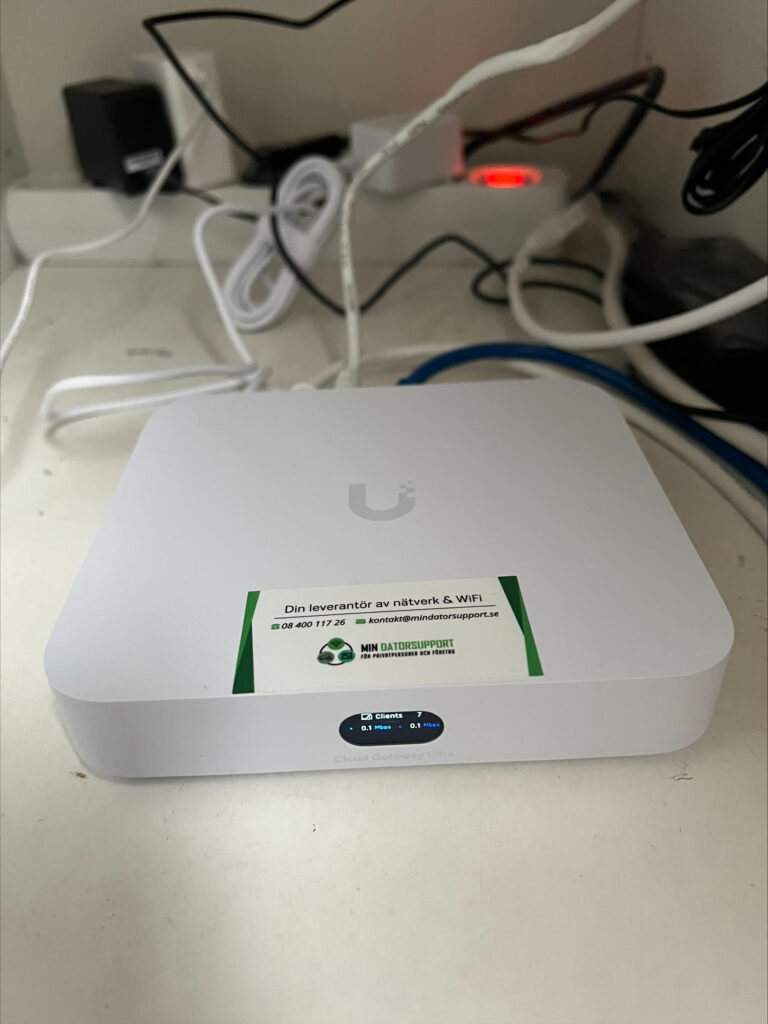 UniFi Cloud Gateway Ultra på en hylla med Min Datorsupports dekal, displayen visar sju anslutna enheter