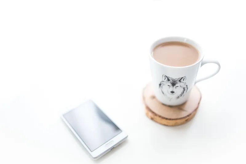 Mobiltelefon och en kopp kaffe på ett vitt bord
