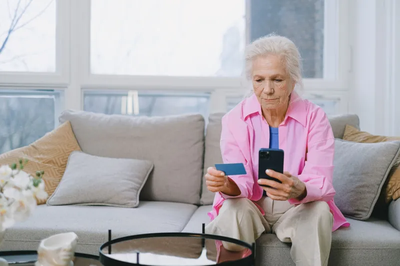 Äldre kvinna använder mobilen hemma i soffan